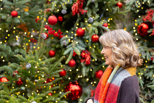 Senior woman smiling by christmas tree decorations