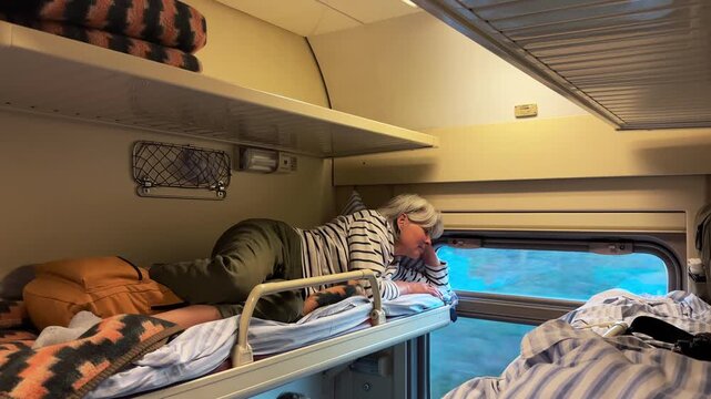 An adult woman resting on the upper berth of a train compartment and looking out the window, travel agency, tourism industry, vacation journey, railway travel.