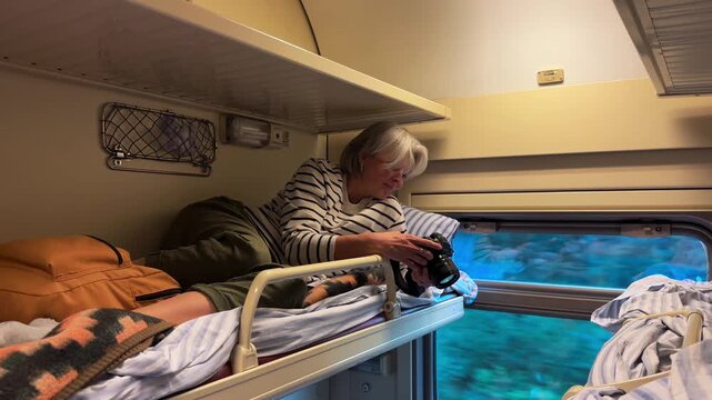 An adult woman lying on the upper bunk bed of a train compartment and looking at her smartphone, travel agency, tourism industry, vacation journey, mobile communication.
