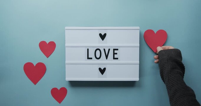 Person holding a light box that spells love on a blue background with hearts hands lightbox message sign romance