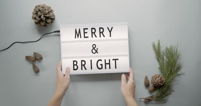 Hands holding merry and bright message cinema light box decoration with pine cones lightbox christmas holiday seasonal