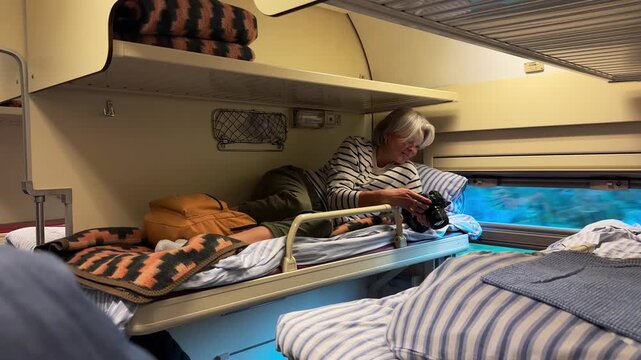 A mature woman lying comfortably on the upper shelf of a train compartment while using her smartphone, travel agency, tourism industry, vacation journey, digital connectivity.