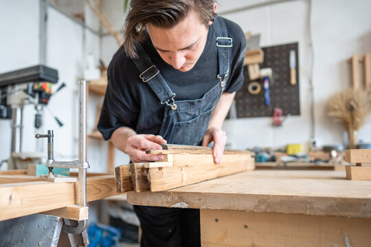 Talented man carpenter renovating vintage wooden frame, precisely picks wooden patch for replacement, preparation work for old window frame restoration, selection of material same type and hardness.