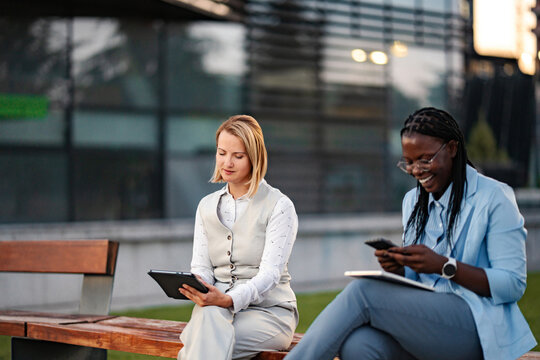 Two businesswomen using digital tablets and smartphones outdoors in a professional setting