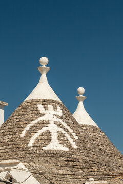 Trullo conical roofs with white spherical pinnacles and painted symbol against clear blue sky in Alberobello