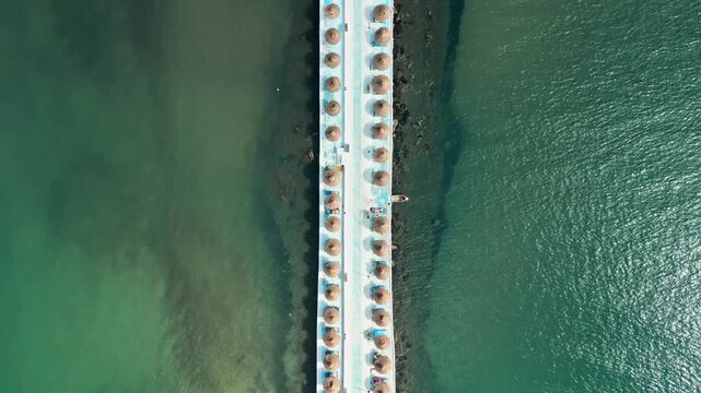 Albania, Durres 07 09 2025: Symmetrical top-down drone video moving forward along a pier pathway over the sea until revealing the Hawaii Beach Club in the center.