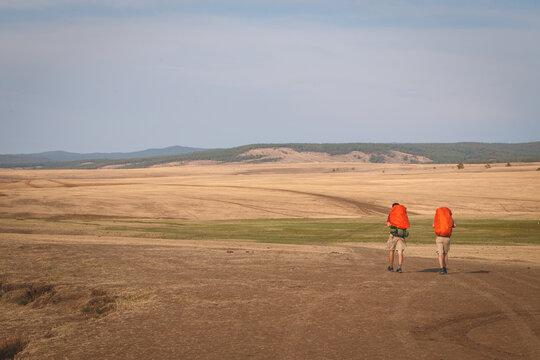 Two hikers with backpacks walking on trail against hills on Olkhon Island, Lake Baikal, Siberia