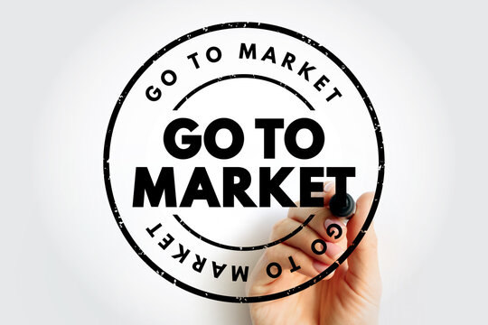 GO TO MARKET text in a circular rubber stamp held by a person. Business strategy for product launching and sales planning