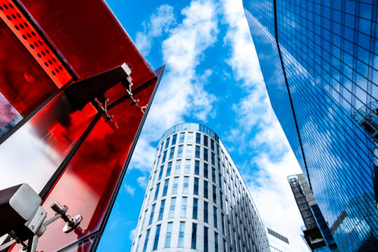 A red structure cuts across glass office towers in Warsaw, Poland, while corporate architecture energizes the business district with upward perspective