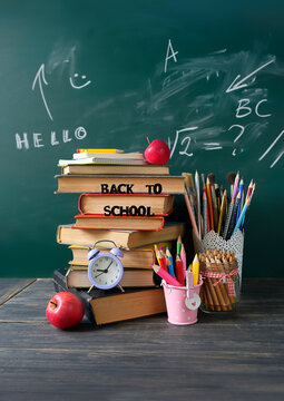 back to school concept. set of stationery, apples, alarm clock and stack of learning books on table against chalkboard. symbol of beginning of the school year, Knowledge Day, education,1 September