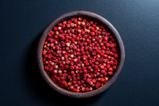 Fresh wild strawberries in a rustic clay bowl, closeup. Top view of round ceramic dish filled with large amount of ripe red forest wild strawberries placed on dark background with shadows