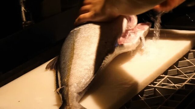 A professional chef cleans and cuts whole fish on a cutting board using sharp kitchen tools for culinary preparation in a commercial restaurant setting