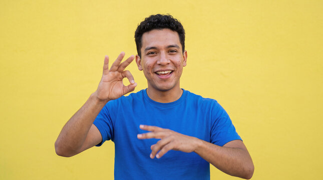 Man communicating in sign language making ok gesture against a yellow background