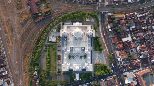 Aerial view of Sheikh Zayed Grand Mosque Solo with white domes and courtyard architecture surrounded by urban streets and railway tracks in Kecamatan Banjarsari, Jawa Tengah, Indonesia.