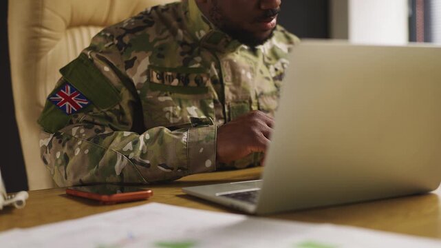 Black British ranking army officer manages security operation, typing on laptop