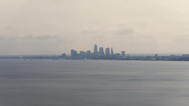 Cleveland, OH skyline with cloudy moody sky above on overcast summer day as tall buildings, skyscrapers, office building, and structures in silhouette stand over Lake Erie on Ohio coastline 4k