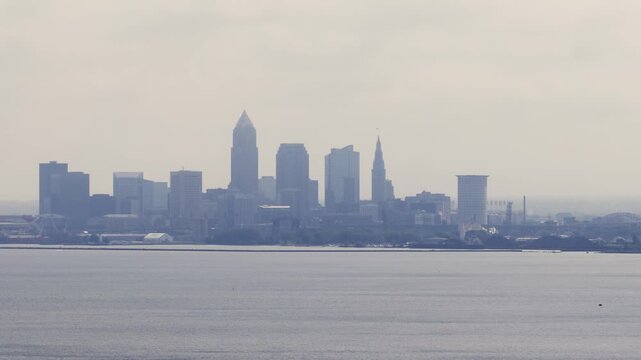 Cleveland, OH skyline with cloudy moody sky above on overcast summer day as tall buildings, skyscrapers, office building, and structures in silhouette stand over Lake Erie on Ohio coastline 4k