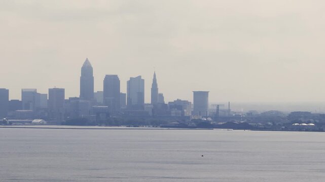 Cleveland, OH skyline with cloudy moody sky above on overcast summer day as tall buildings, skyscrapers, office building, and structures in silhouette stand over Lake Erie on Ohio coastline 4k
