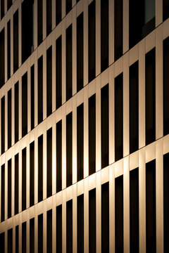 Warm sunlight crosses a modern architecture facade, where vertical fins, windows, contrast and repetition build a precise pattern with measured rhythm.