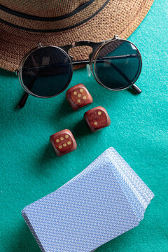 Playing cards, wooden dice, sunglasses and a hat on a green cloth.