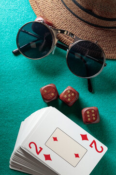 Playing cards, wooden dice, sunglasses and a hat on a green cloth.