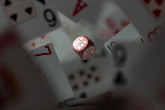 Wooden die in motion surrounded by playing cards.