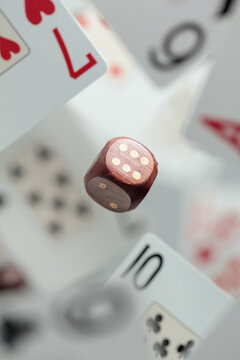 Wooden die in motion surrounded by playing cards.
