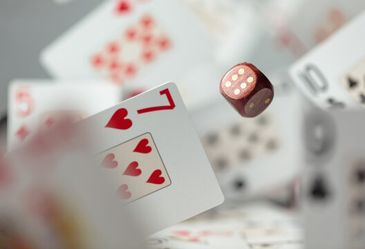 Wooden die in motion surrounded by playing cards.