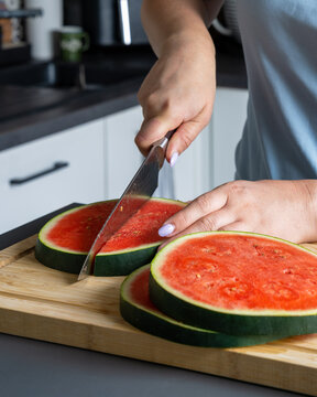Woman halving round watermelon slices on wooden board