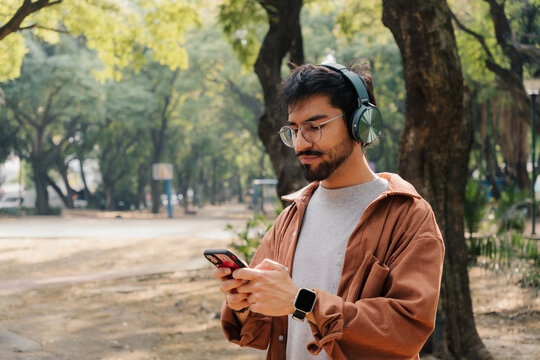 Young man in corduroy shirt using mobile phone in sunny park