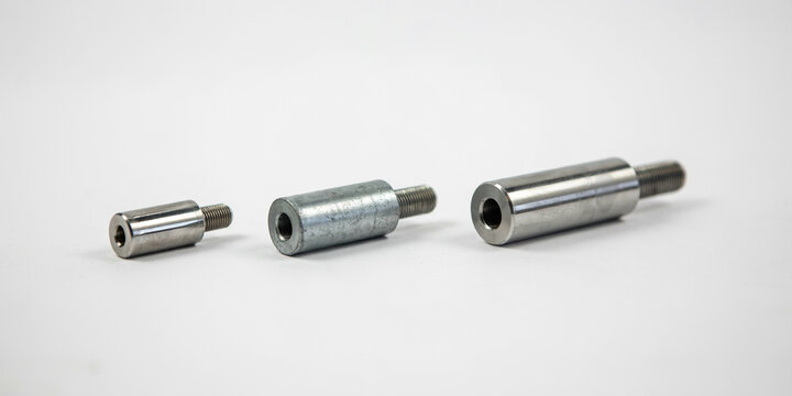 Three cylindrical metal studs with threaded ends and hexagonal holes on white