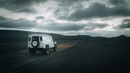An off-road vehicle drives across the remote volcanic plains near Mælifell, surrounded by black lava fields, dramatic storm clouds and the rugged beauty of Icelandic Highlands in pristine wilderness. © Jag_cz