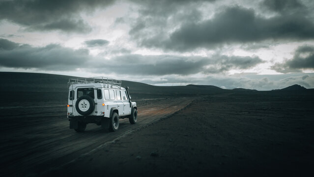 An off-road vehicle drives across the remote volcanic plains near M&aelig;lifell, surrounded by black lava fields, dramatic storm clouds and the rugged beauty of Icelandic Highlands in pristine wilderness.