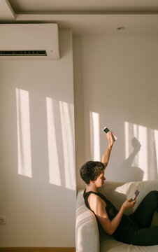 A woman turns on the air conditioner while looking at her phone 