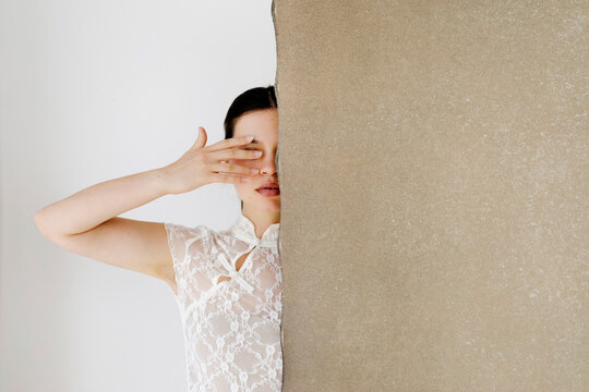 Woman hiding face behind textured wall