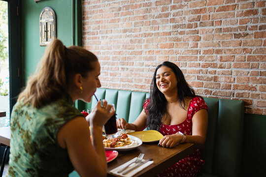 Happy woman laughing with her friend over dinner at a cozy eatery