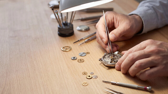 Faceless watchmaker hands repairing mechanical wristwatch with precision tweezers, craftsmanship concept with copy space
