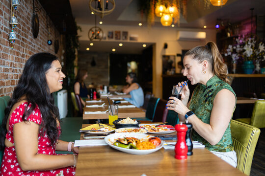 Two young women chatting and drinking sodas at a restaurant table