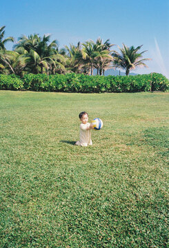 Young child kneeling on green grass holding a colorful ball