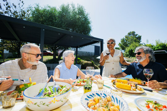 Senior friends enjoying outdoor summer lunch with food and drink