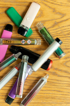 Top view of various colorful disposable vapes with warning pictograms on wood background, illustrating harmful effects of vaping, lung disease risks, and unsafe nicotine consumption habits