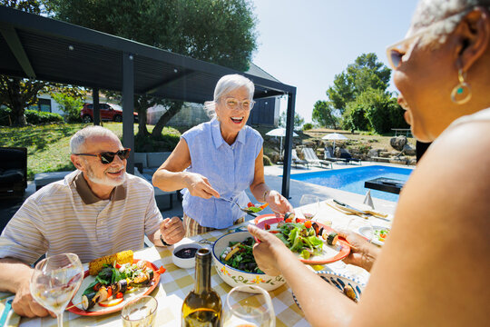 Senior people enjoying healthy meal outdoors by swimming pool