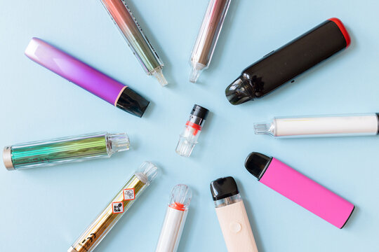 A circular arrangement of colorful e-cigarettes and vape devices on a blue background. This top-down view includes a device with toxic hazard warning labels, highlighting potential health risks.