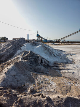Open air sea salt mining site with salt heaps and conveyor machinery under a clear sky