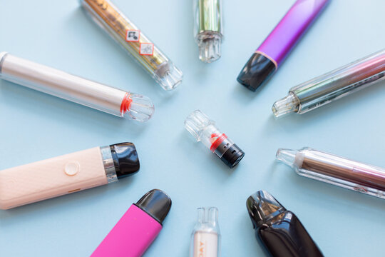 Top view of colorful disposable electronic cigarettes and vape pod arranged in a ring on blue background