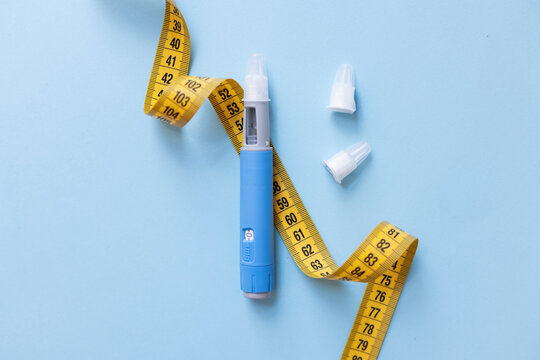 Blue weight loss injection pen with yellow measuring tape on blue background, illustrating dangerous weight loss trends, medication abuse, obesity risks, and severe side effects on health.