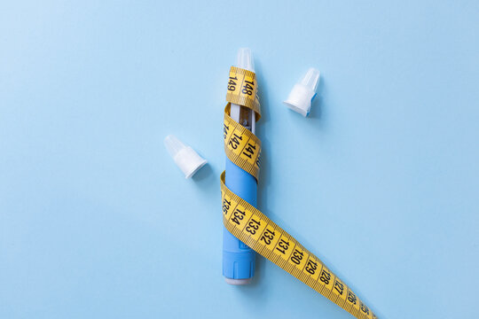 Horizontal view of blue weight loss injection pen wrapped in yellow measuring tape on blue background, showing extreme dieting risks, medication misuse, side effects, and health hazards.