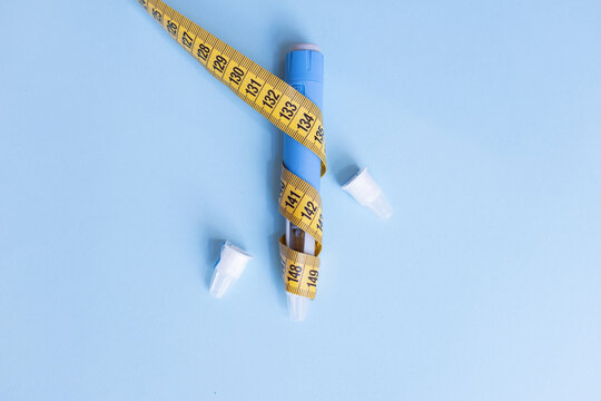Injectable weight loss drug pen wrapped with yellow measuring tape on blue background, highlighting health risks, severe side effects, and dangers of rapid slimming.
