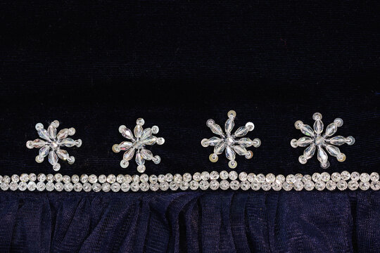 Close up of navy blue velvet fabric decorated with crystal bead star motifs and a double row of shiny clear rhinestones bordering a sheer pleated gathered textile hem for apparel design