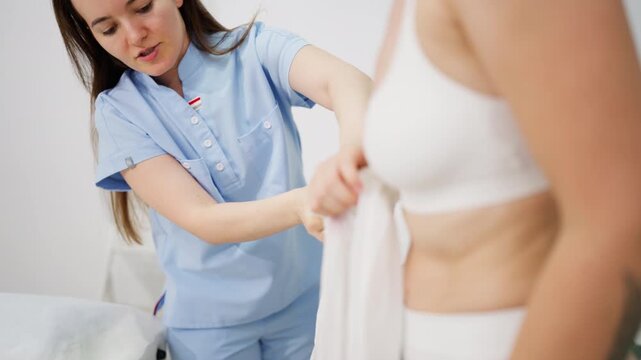 Female client preparing for professional body contouring treatment by putting on a specialized compression suit at an aesthetic beauty clinic.